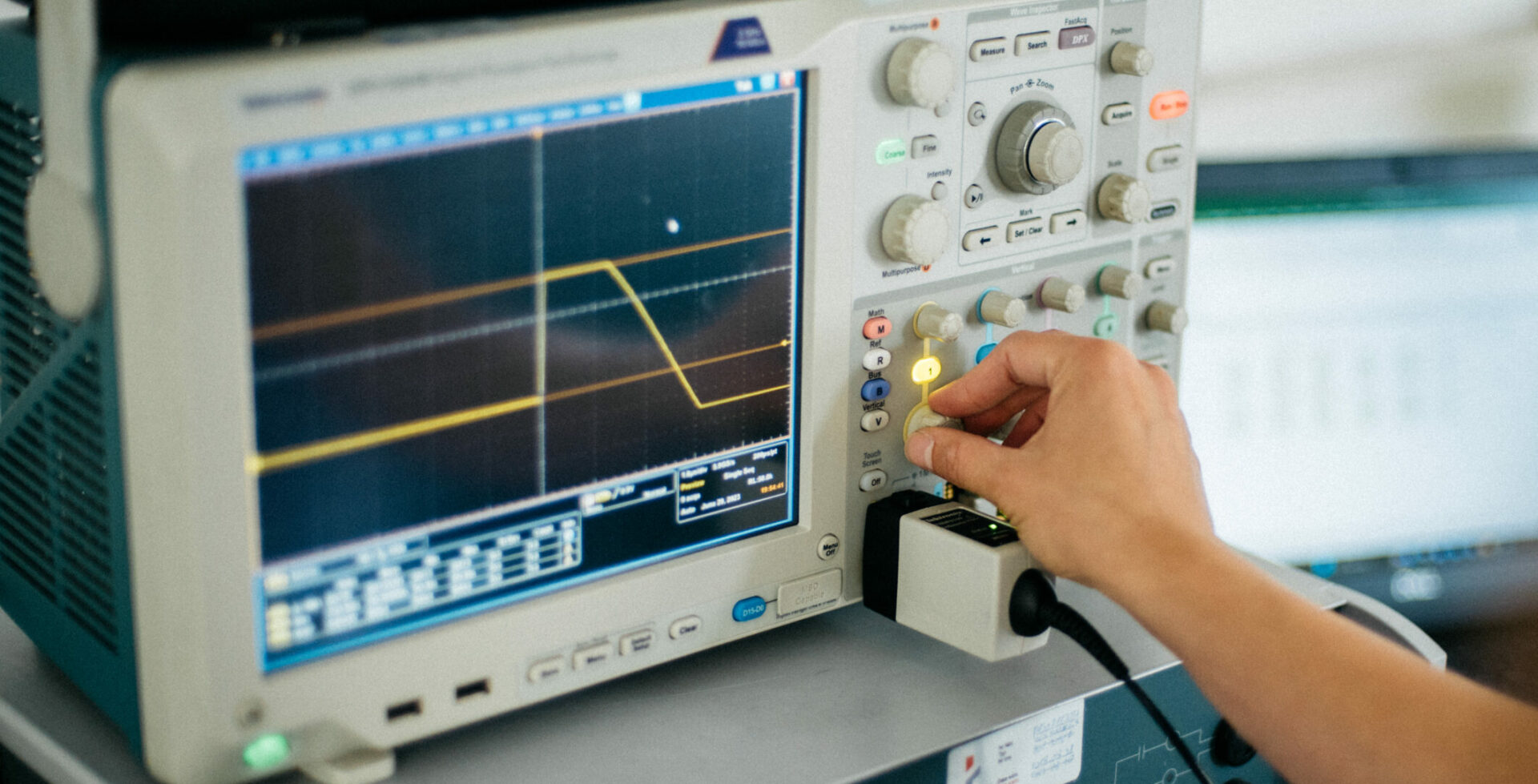 Zbliżenie na laboratoryjne urządzenie pomiarowe. Widoczna dłoń obracająca jedno z pokręteł na panelu sterującym.